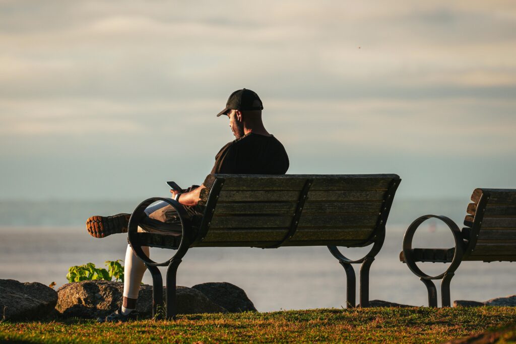 “Homem sentado em um banco observando o mar, representando um momento de reflexão e calma mental.”